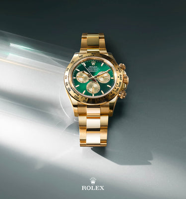 Gold watch with green face on a gray background, featuring the Rolex logo.