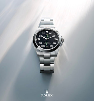 Silver Rolex watch on a reflective gray surface with soft lighting
