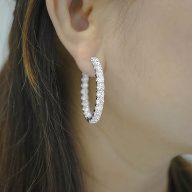 Close-up of a person wearing diamond hoop earrings with blurred background
