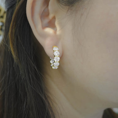 Close-up of an ear wearing a gold earring with clear stones.