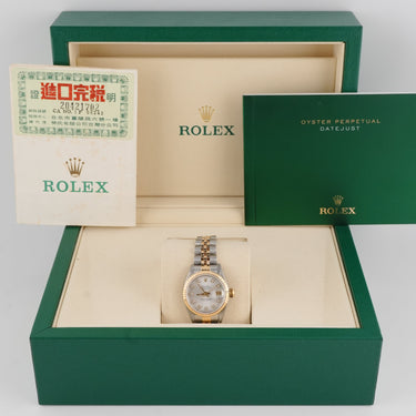 Rolex watch in an open green box with warranty papers on a light gray background